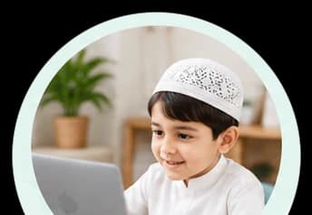 A boy in a prayer cap smiling at his laptop during his lesson at home